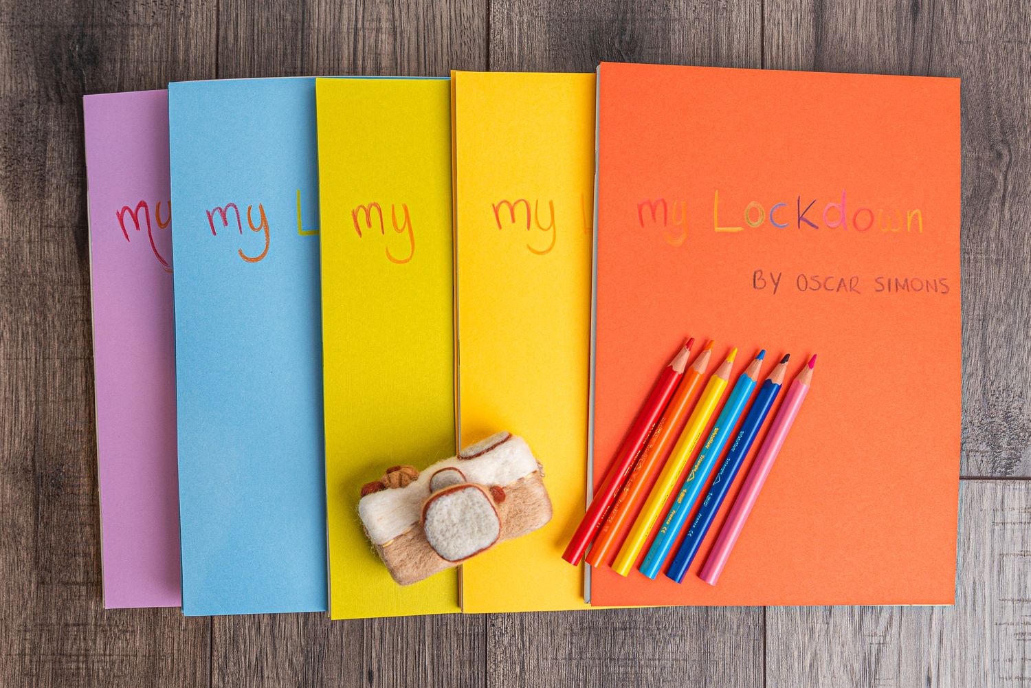 Colorful notebooks with 'My' text and colored pencils arranged on wooden surface.