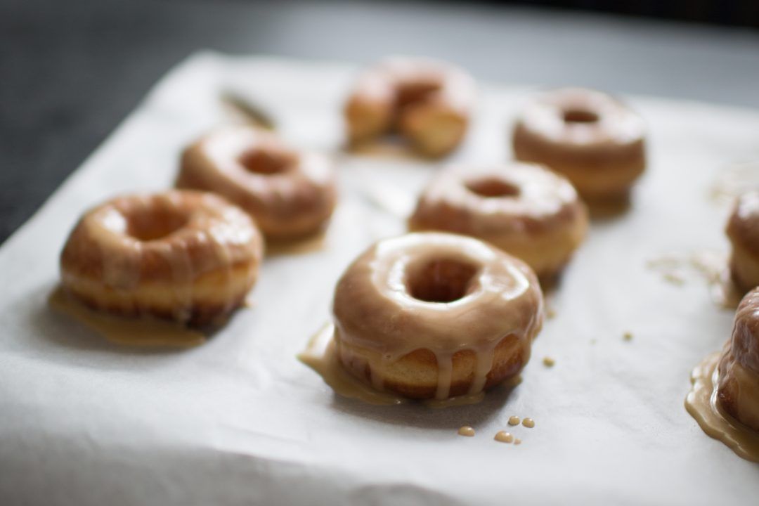Row of glazed mini donuts with caramel coating arranged on white parchment paper.