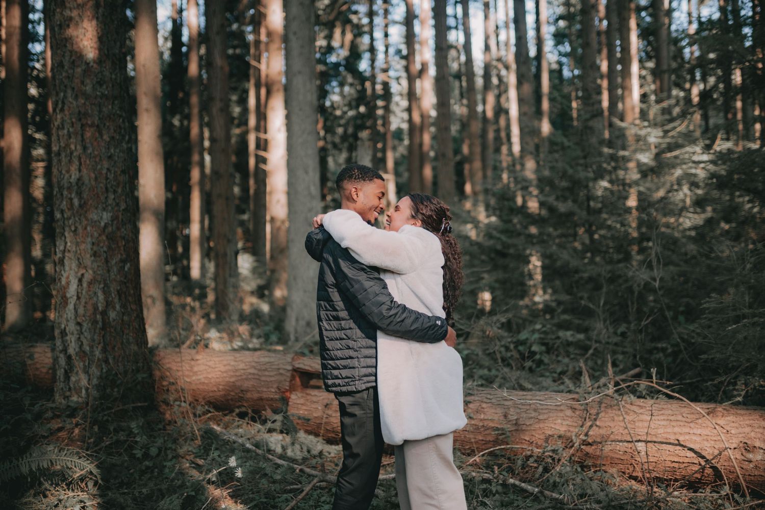 A couple sharing an intimate embrace in a misty forest with tall evergreen trees.
