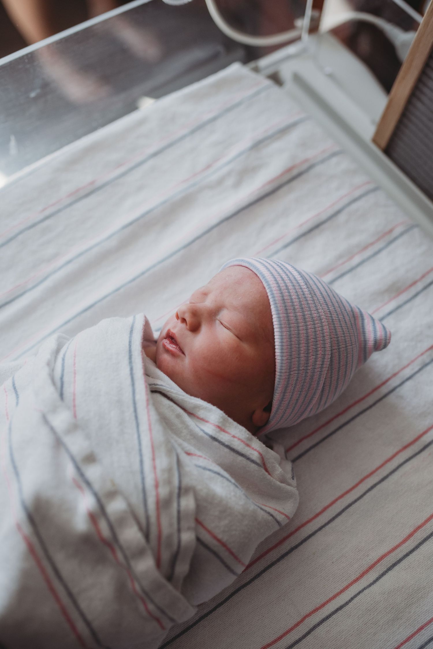 A newborn baby sleeps peacefully swaddled in a white and gray striped blanket.