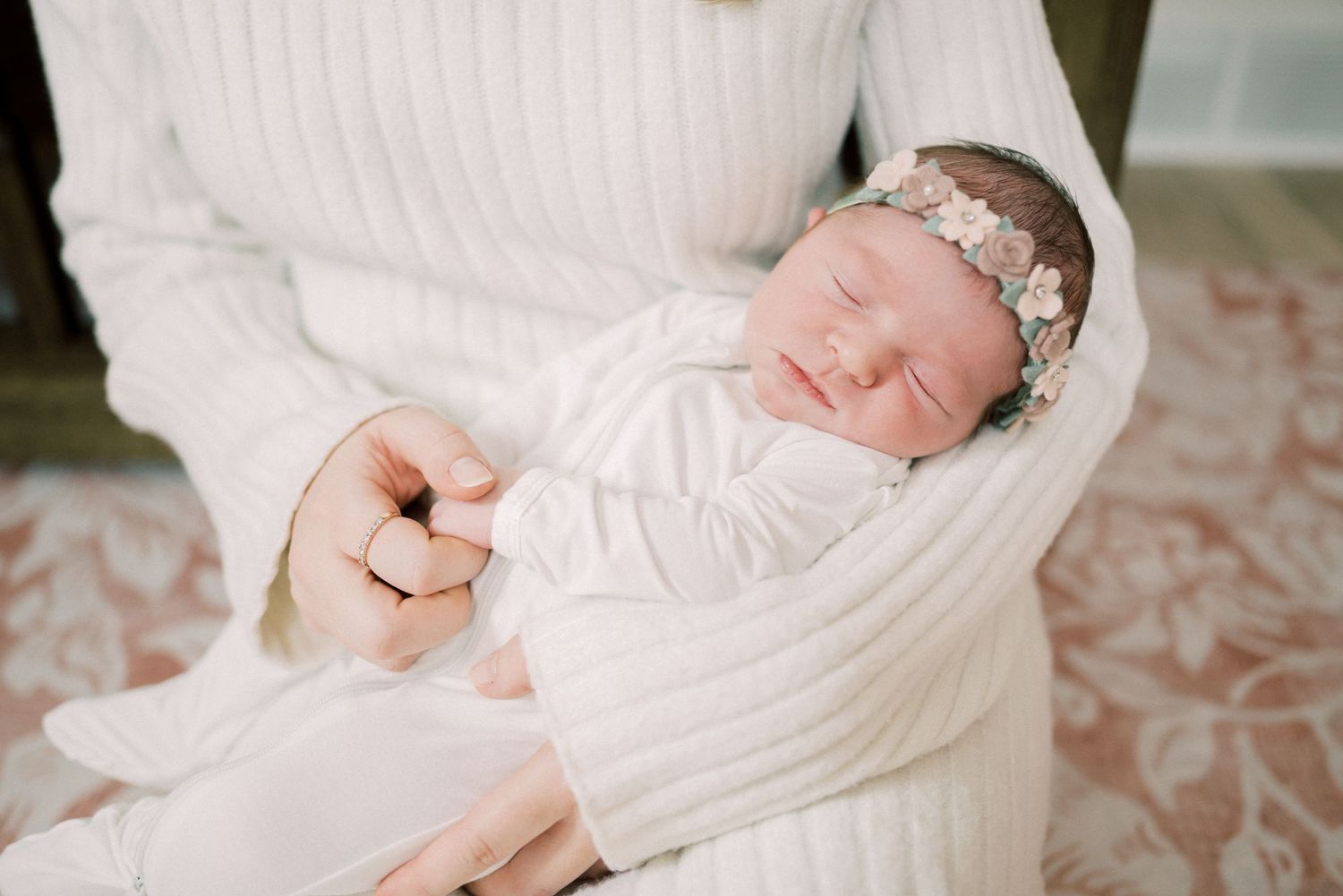 A sleeping newborn in white attire wearing a delicate floral headband.