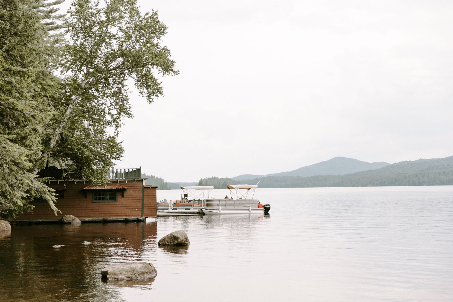 Rustic wooden lakehouse dock with boats on calm water surrounded by evergreen trees.