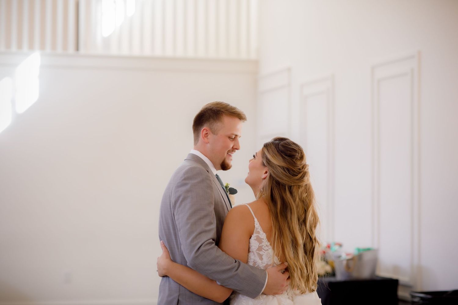 Romantic wedding couple embraces in a sunlit white room.