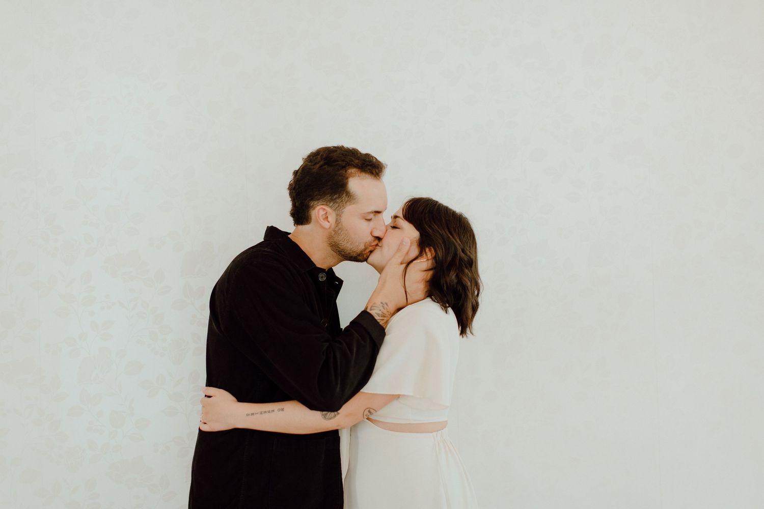 Intimate portrait of couple sharing tender kiss against white wall.