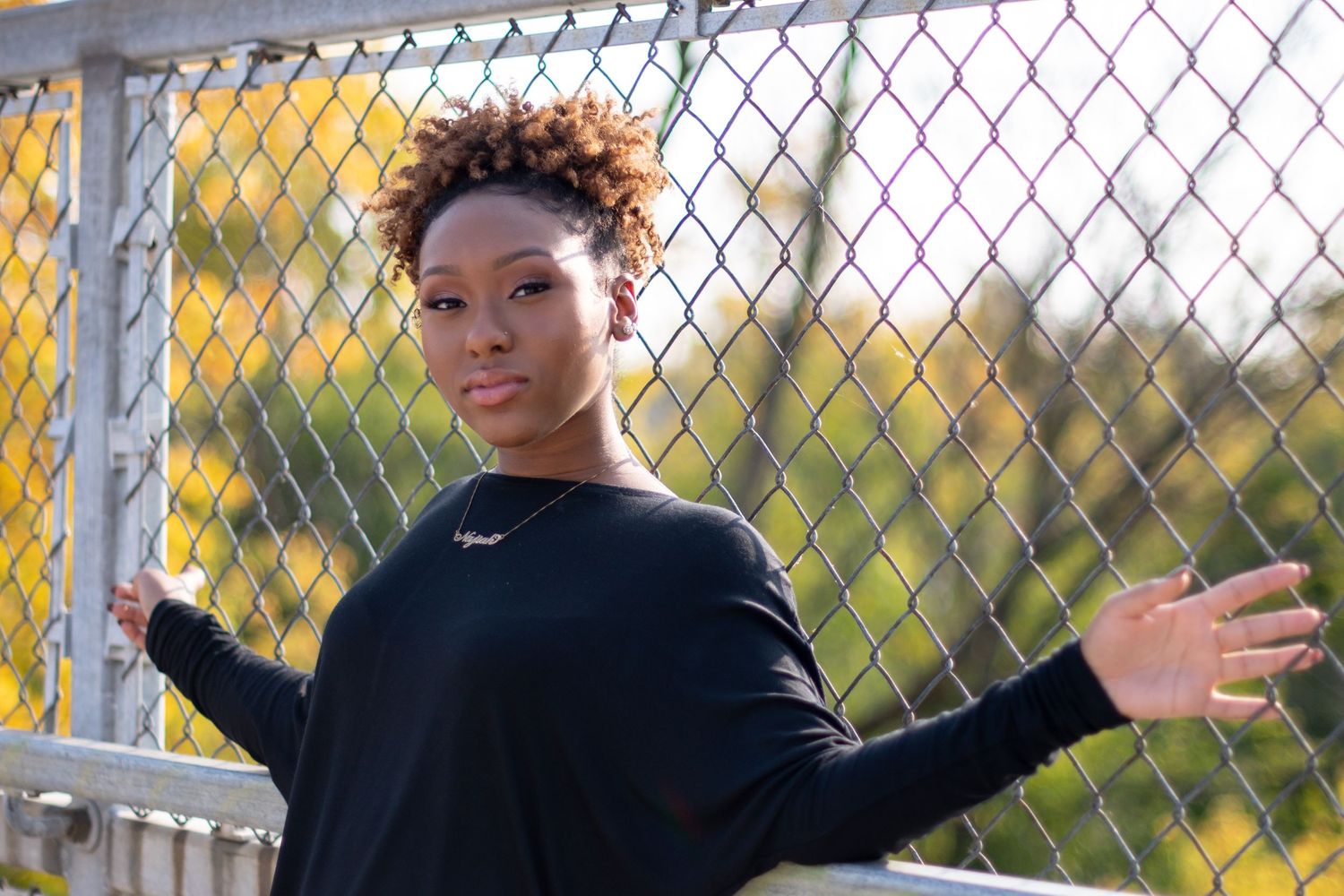 A casual autumn outdoor portrait against a chain link fence with golden sunlight.
