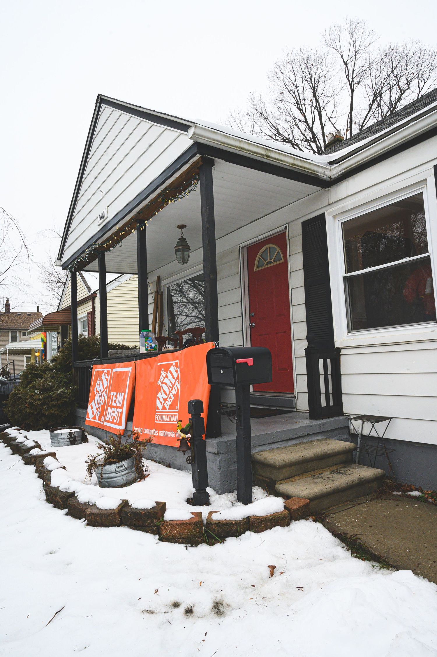 Snow-covered front porch of house with Home Depot delivery boxes by red door.