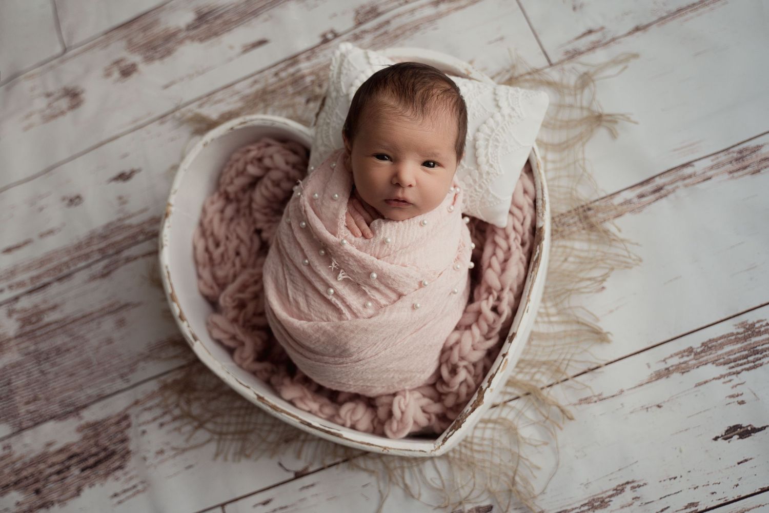 Adorable newborn baby swaddled in pink wrap sleeping in heart-shaped basket with knit blanket.