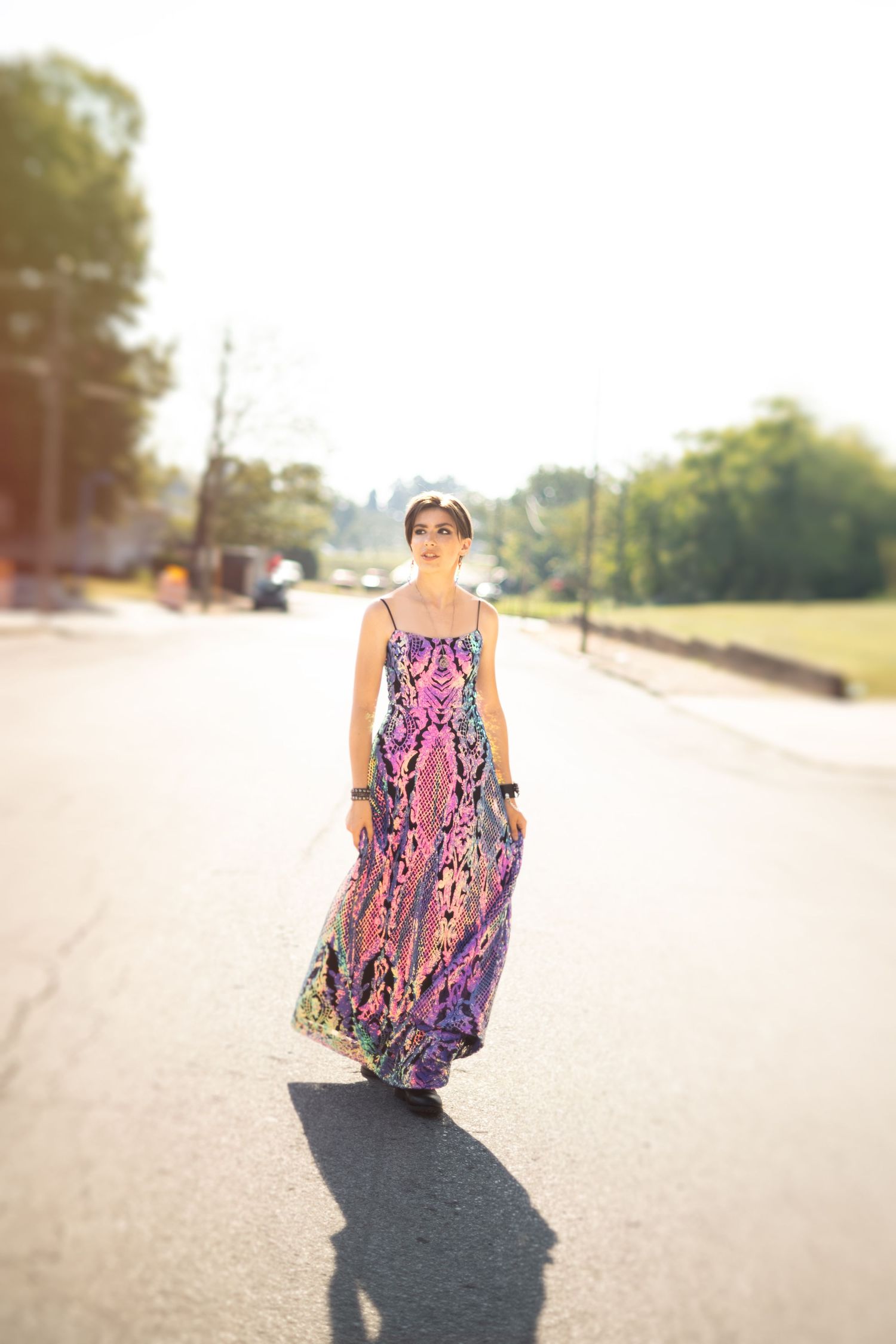 Woman in flowy pink patterned sundress walking down a sunny rural road.