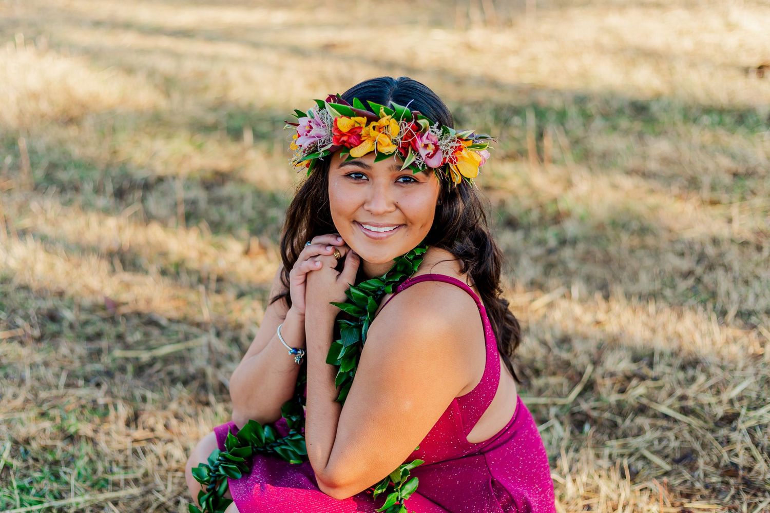 A person wearing a colorful flower crown poses outdoors in a pink dress.