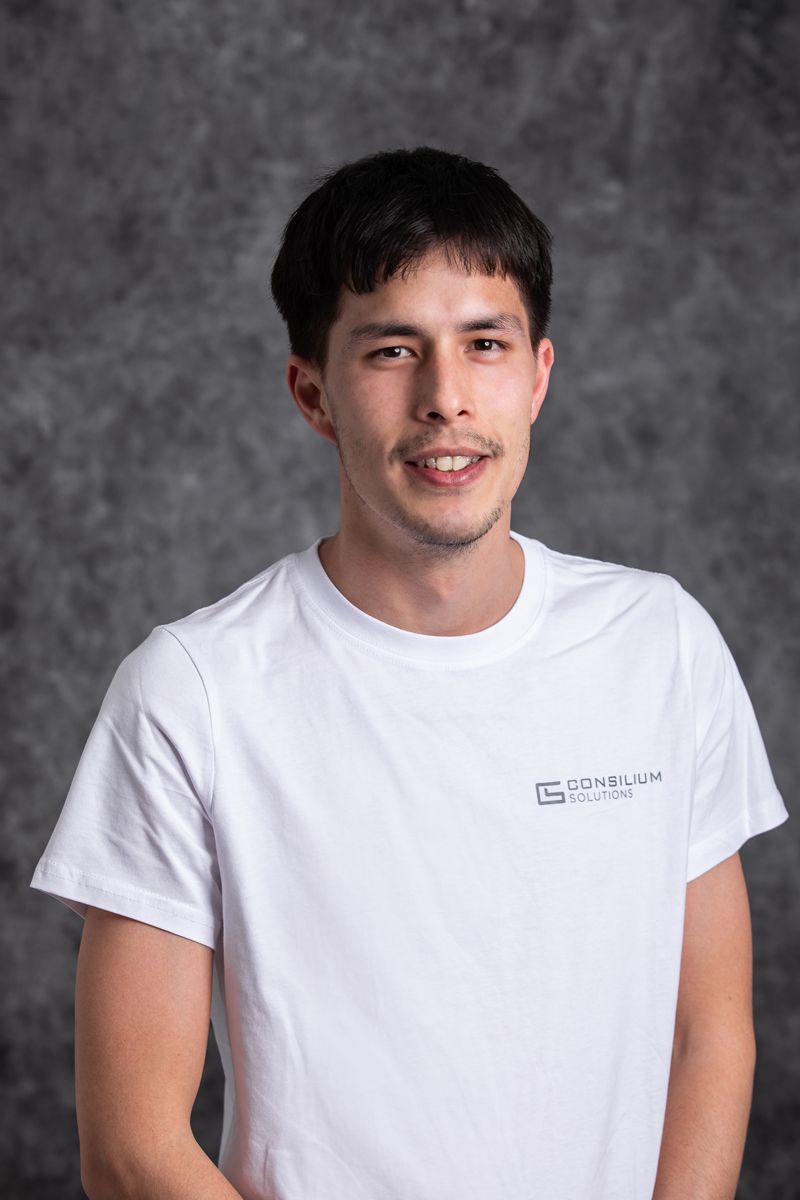 Portrait shot of person in white t-shirt with company logo against grey backdrop.