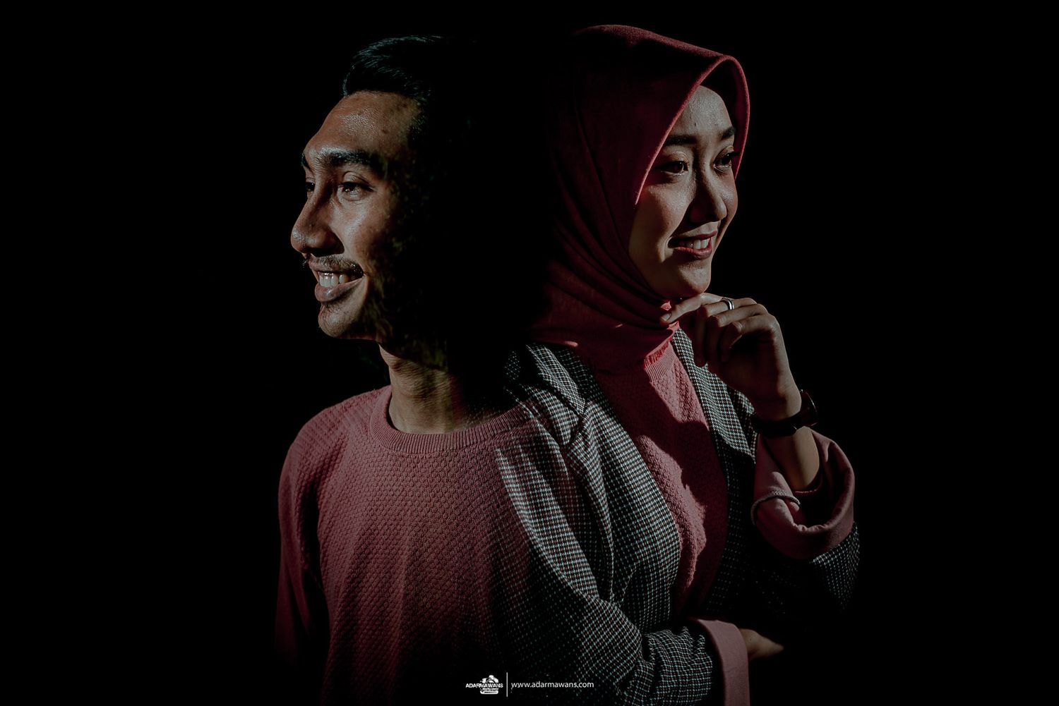 Dramatic low-key portrait of a couple in casual wear against a black background.