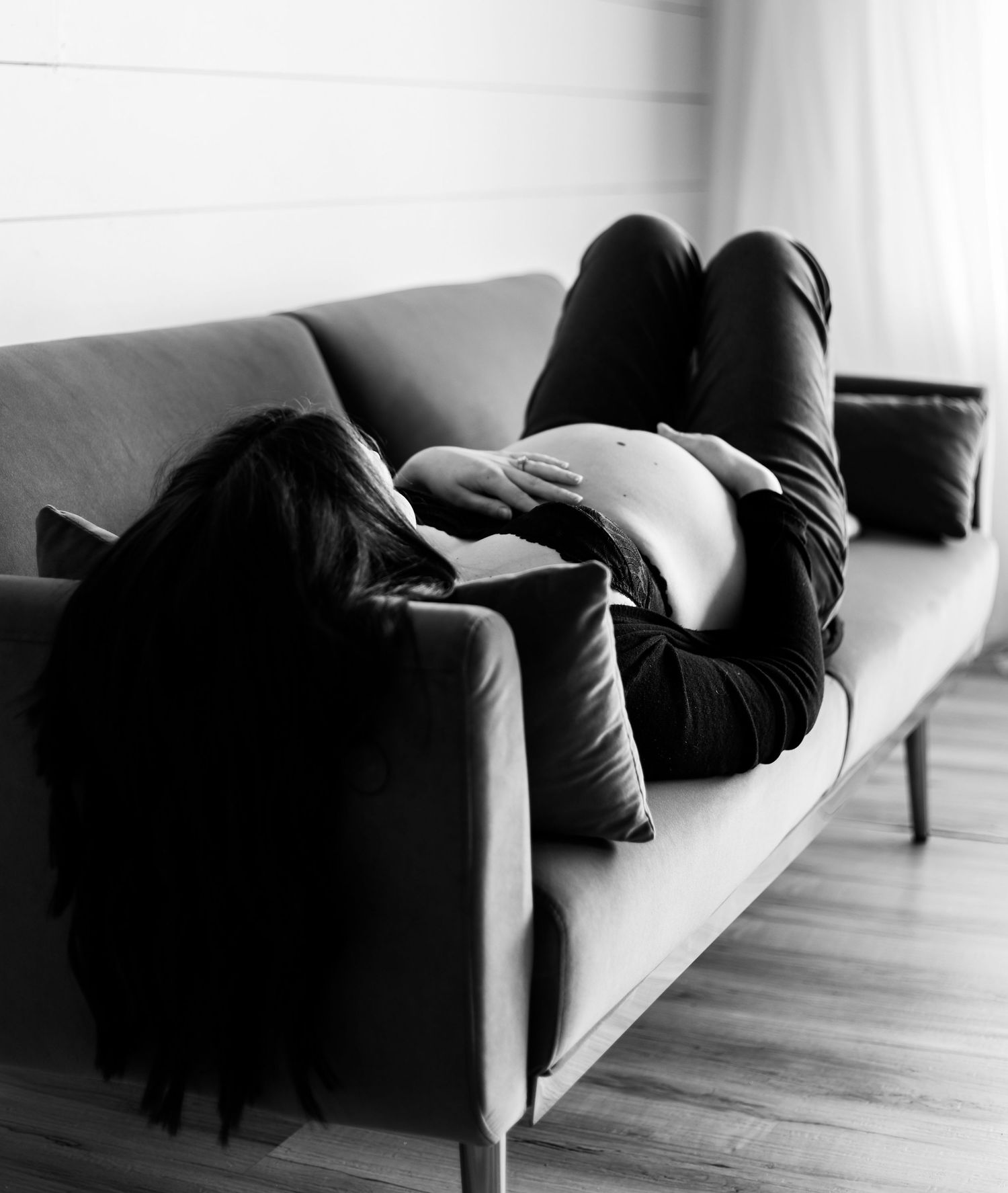 Artistic black and white photo of someone resting on a modern grey sofa in natural light.