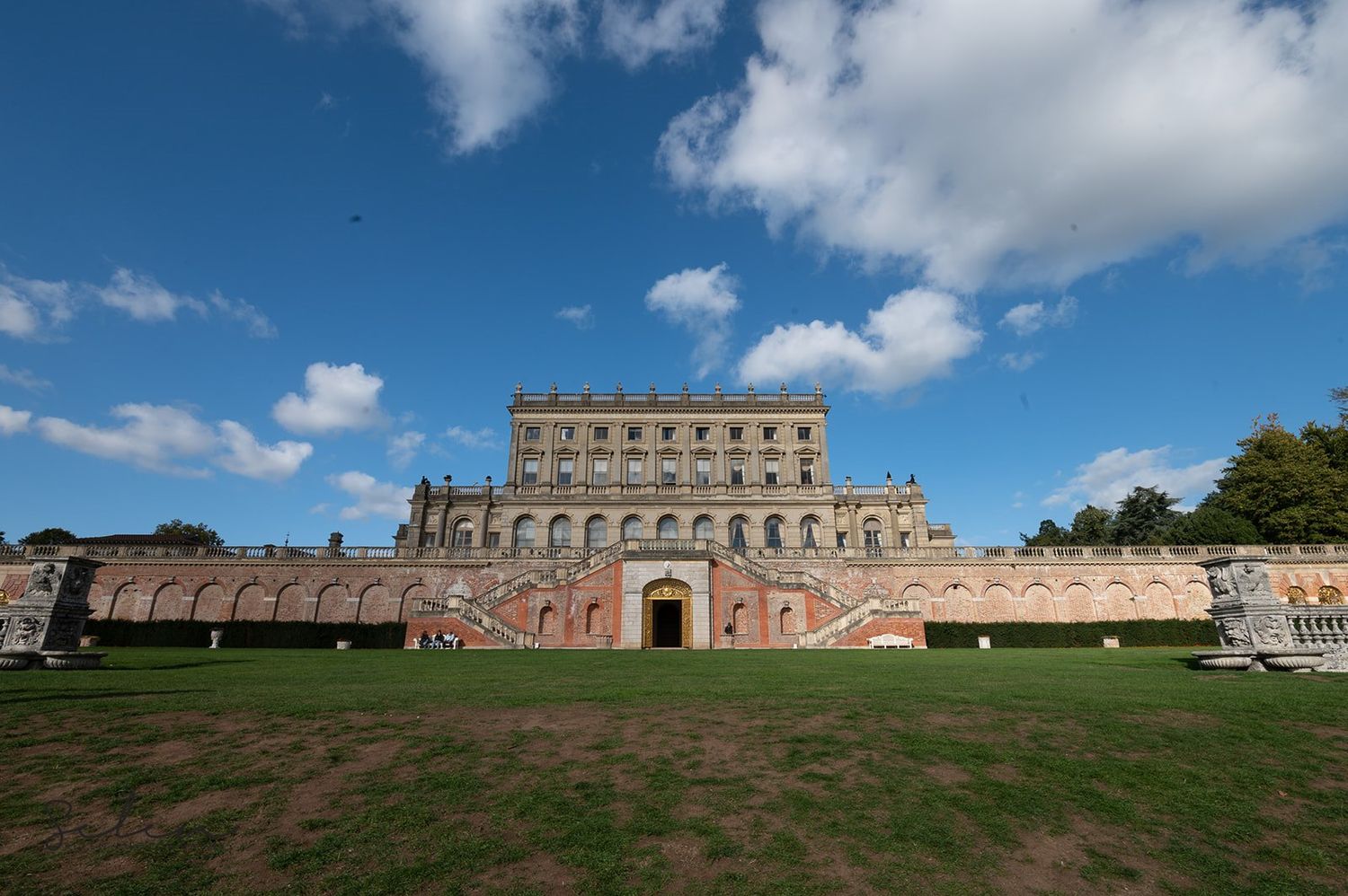 Historic stone mansion with grand architecture photographed under blue skies with white clouds.