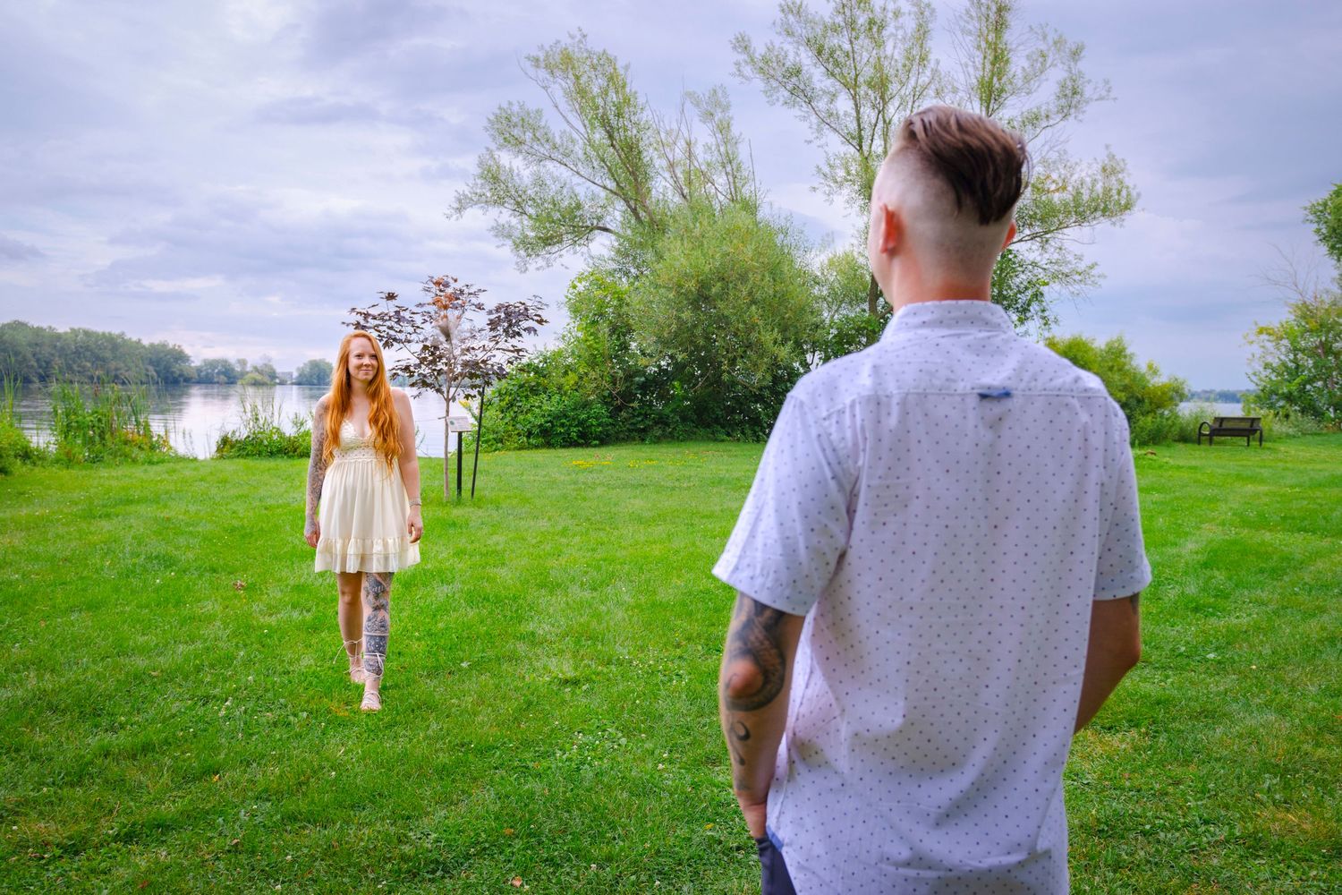 Two people meeting in a green field with trees and cloudy sky in the background.