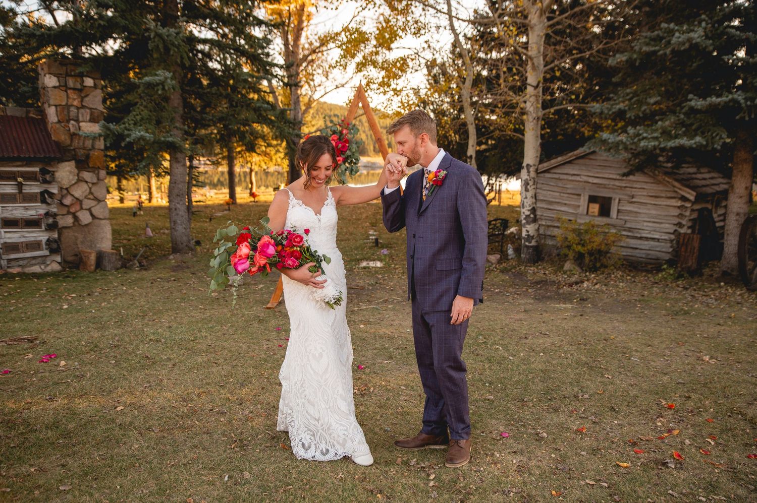 A couple in wedding attire sharing a moment in a rustic outdoor setting at sunset.