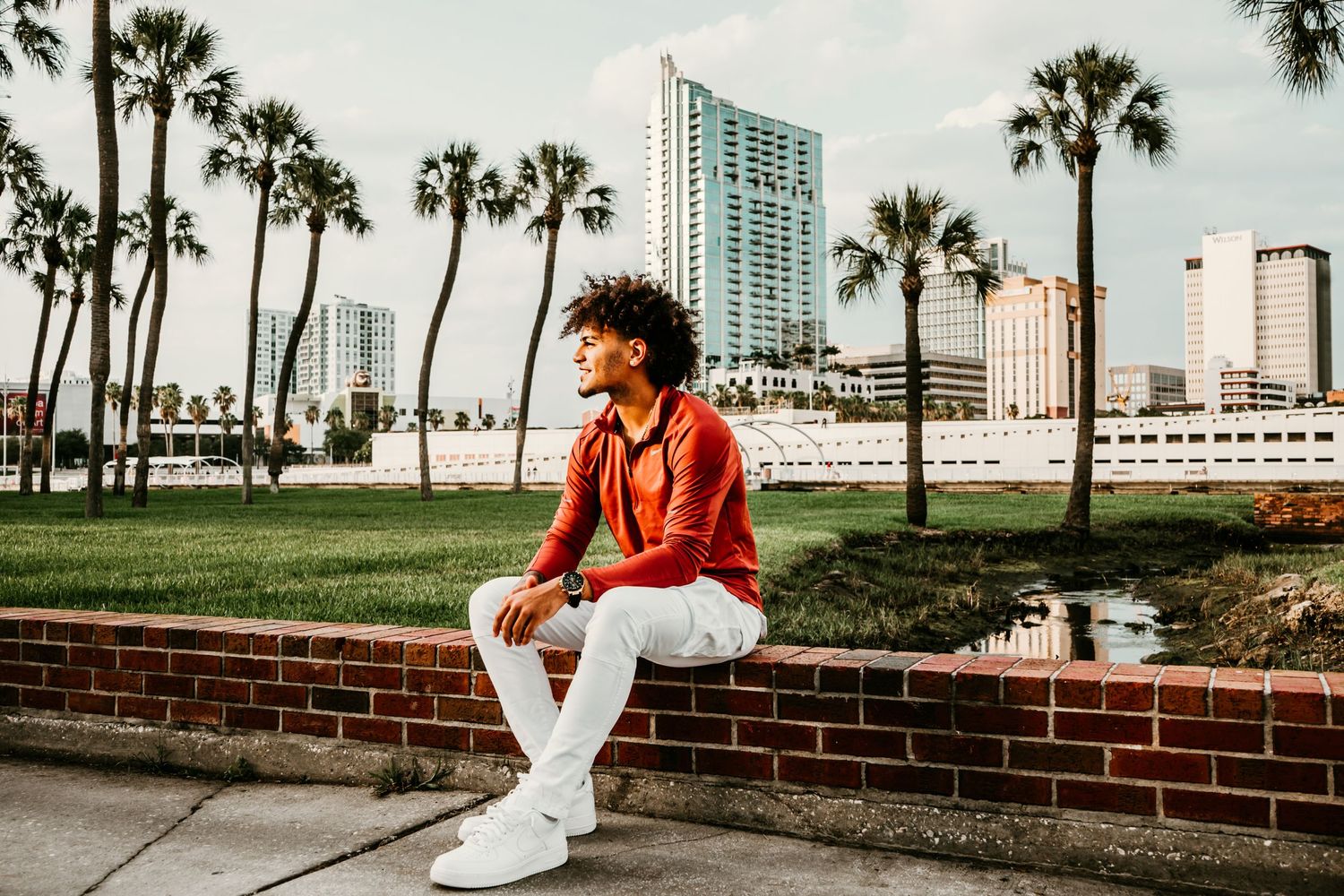 Outdoor Senior Portrait Session at University of Tampa in Tampa, FL; Senior pictures, teen sitting on brick wall with city backdrop