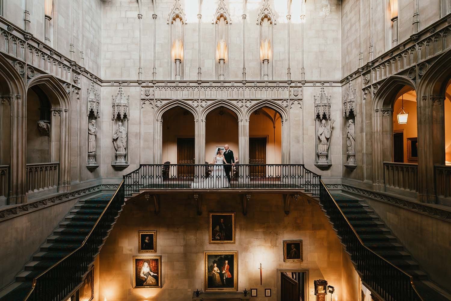 Grand historic staircase with gothic architecture illuminated by warm chandelier lighting.