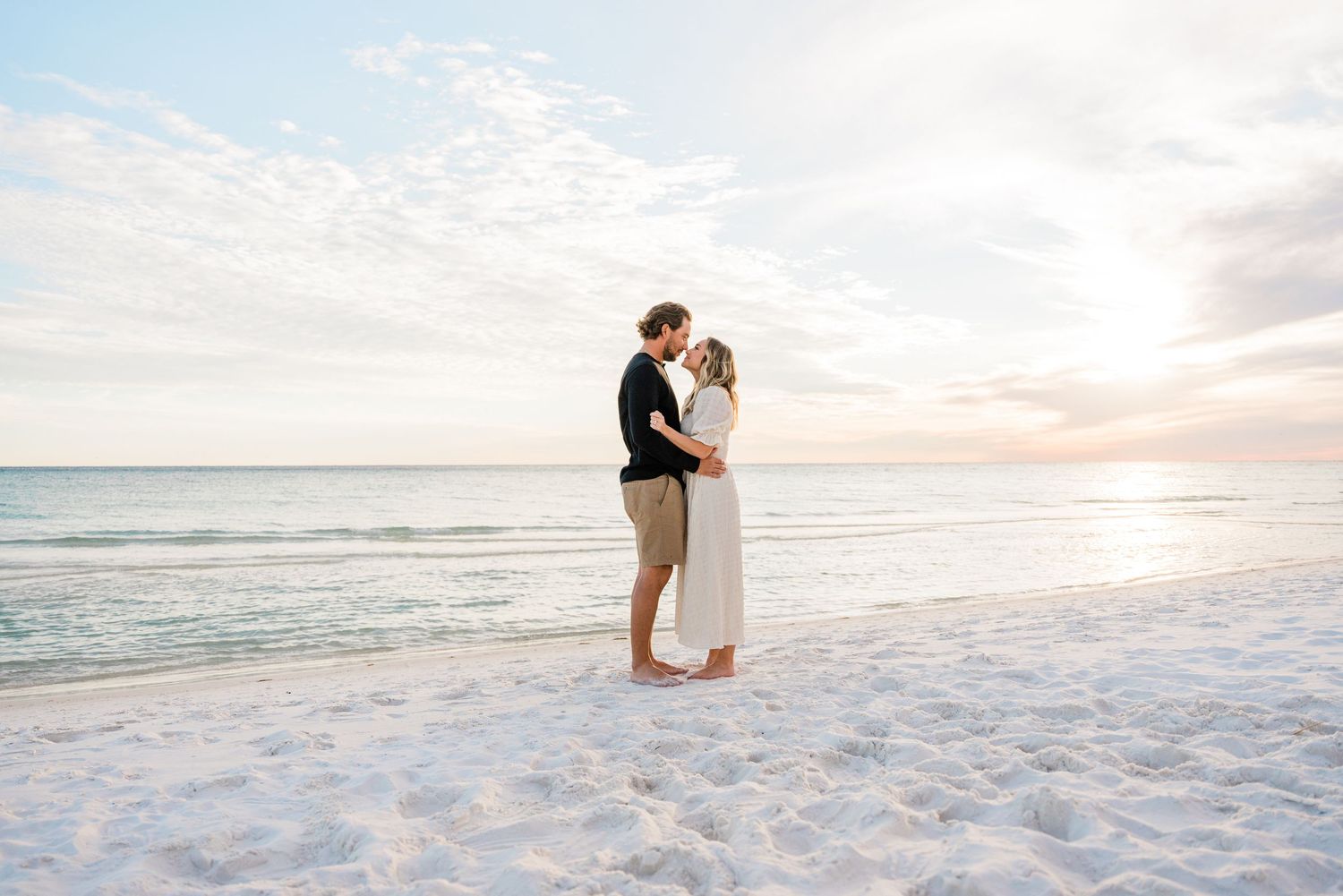 A couple shares an intimate moment on a pristine white sand beach at sunset.