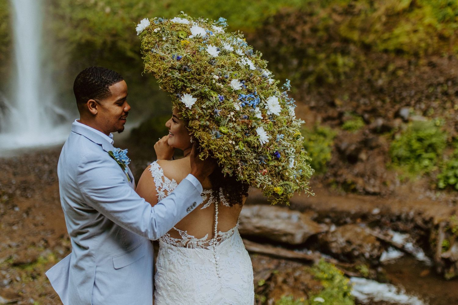 Wedding photoshoot by a scenic waterfall with natural greenery.