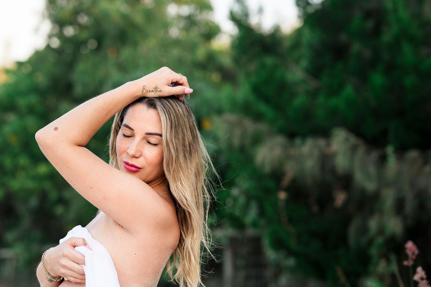Expectant mother in white dress poses outdoors during golden hour.