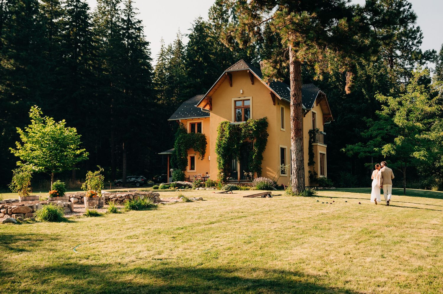 Charming yellow cottage-style house with ivy covered walls surrounded by evergreen trees.