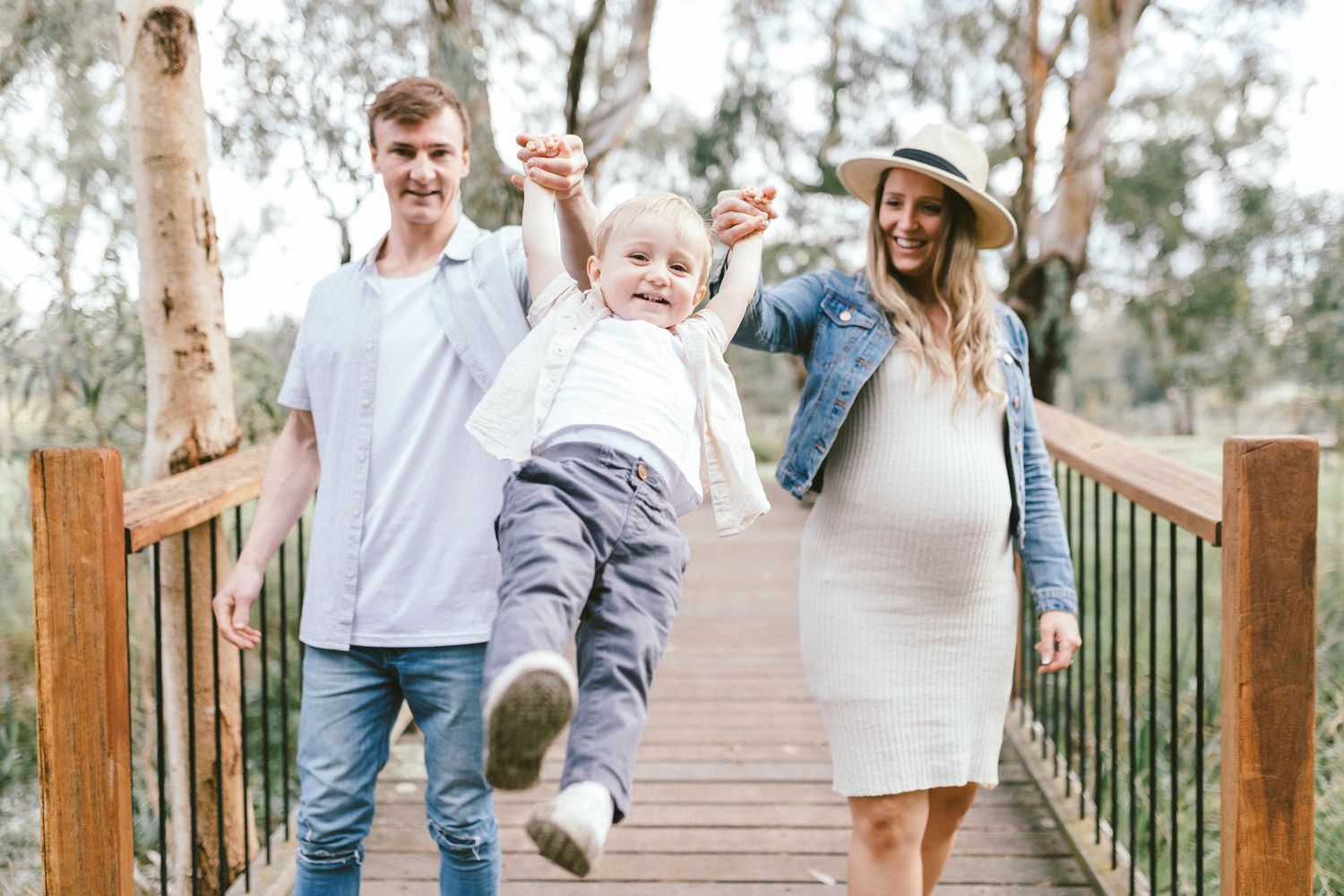 Family enjoying a playful moment on a wooden boardwalk surrounded by eucalyptus trees.