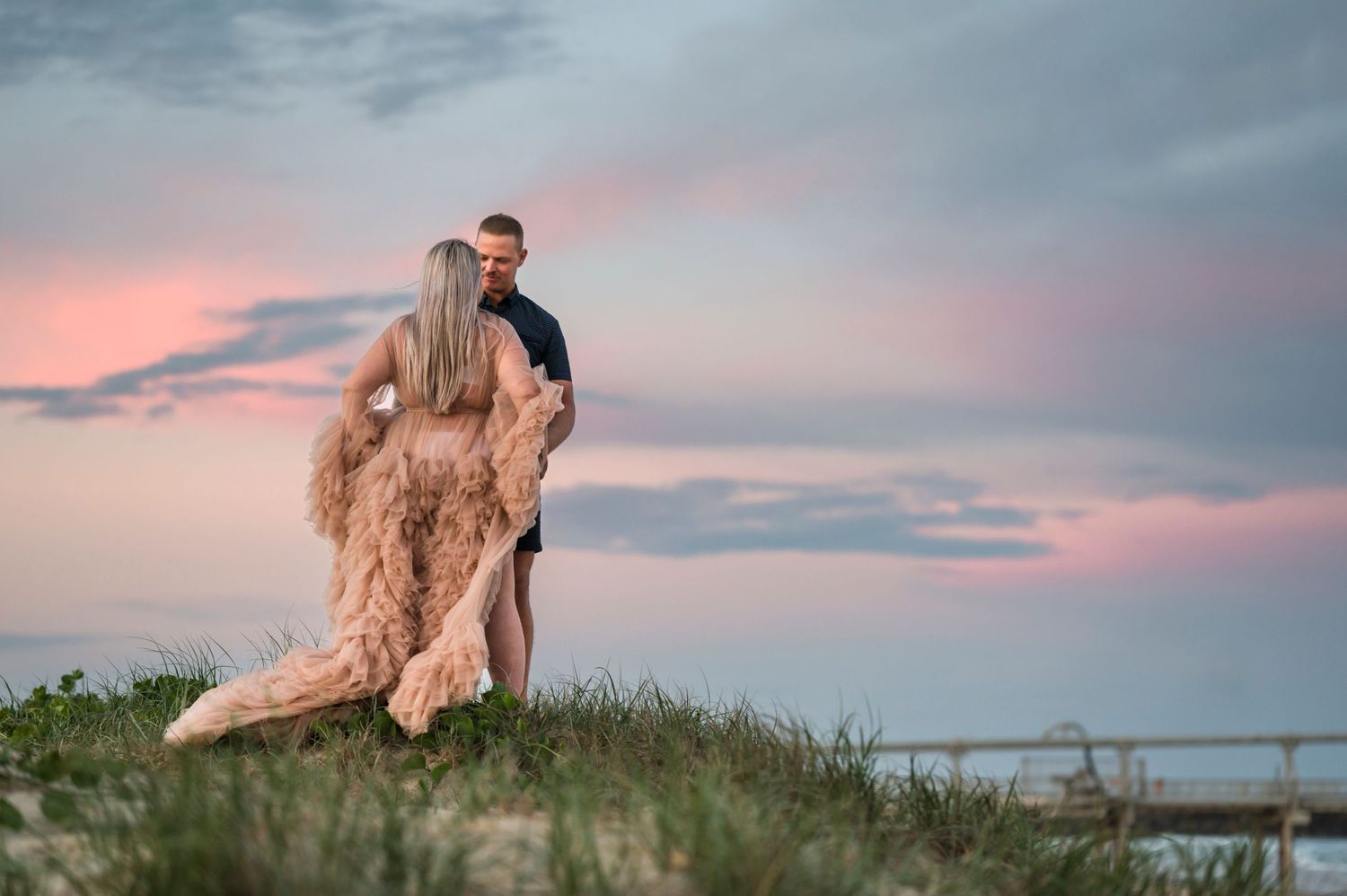 A romantic silhouette of a couple on a hilltop against a pink sunset sky.