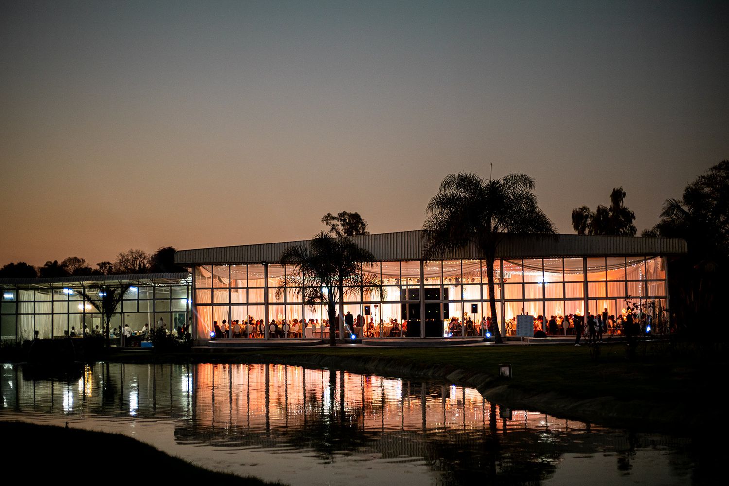 Wedding venue lit up at dusk with glowing windows reflecting in still water.