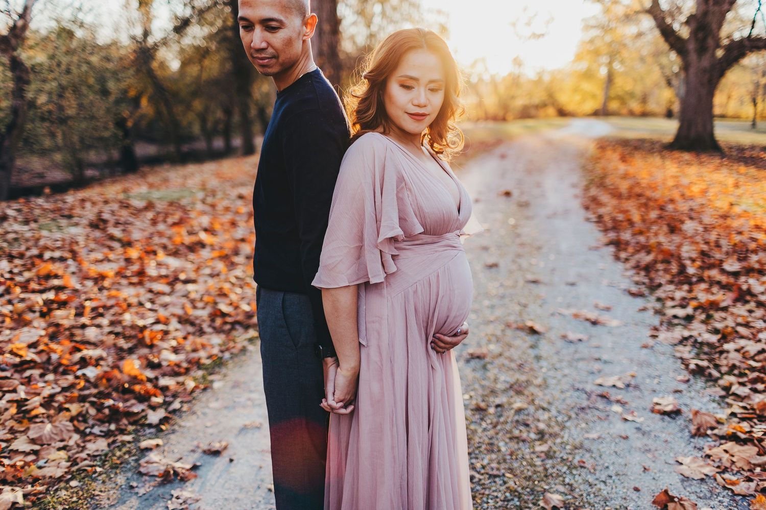 Loving couple shares intimate moment on path surrounded by autumn foliage at sunset.