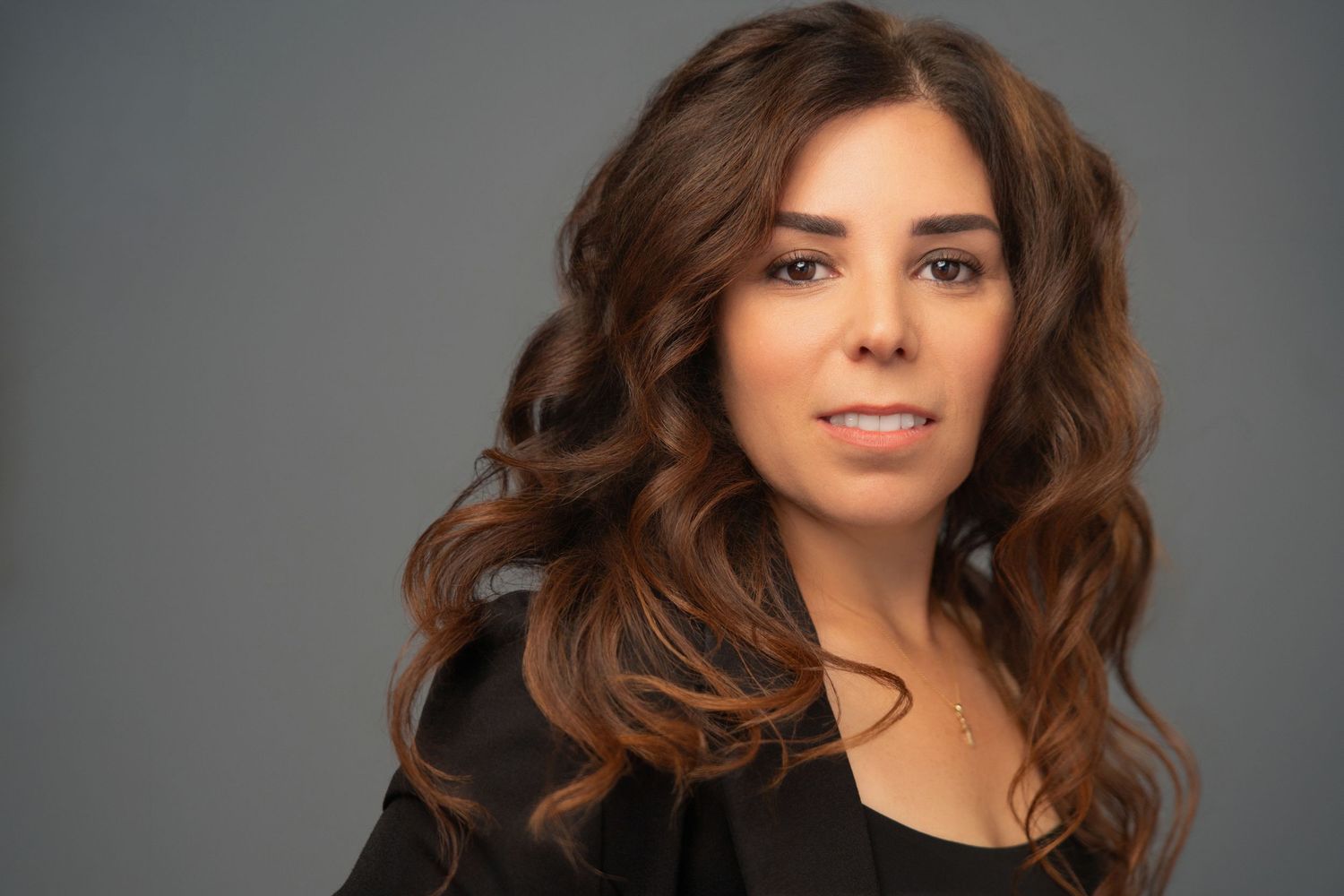 Smiling businesswoman with curly hair sitting at desk with laptop, resting chin on hand in modern office.