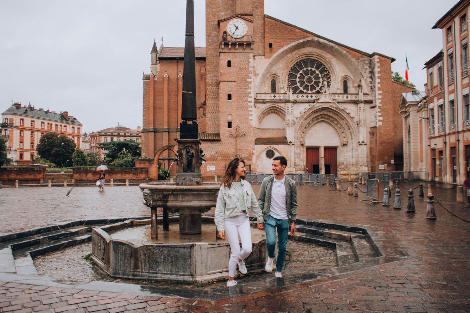 A couple sits on a fountain edge in front of a historic church on a rainy day.