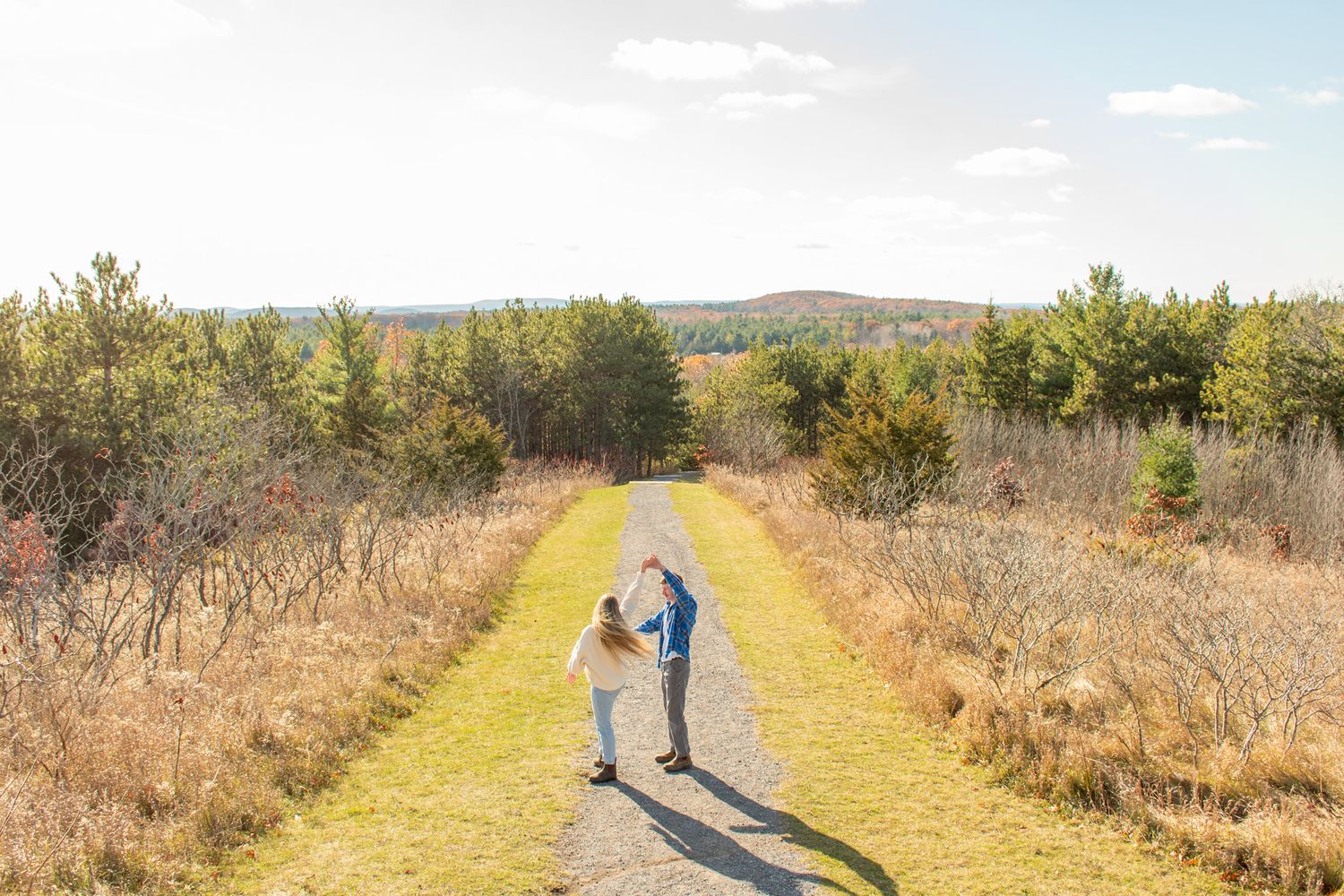 A distant view of two people walking together on a winding trail through open countryside.