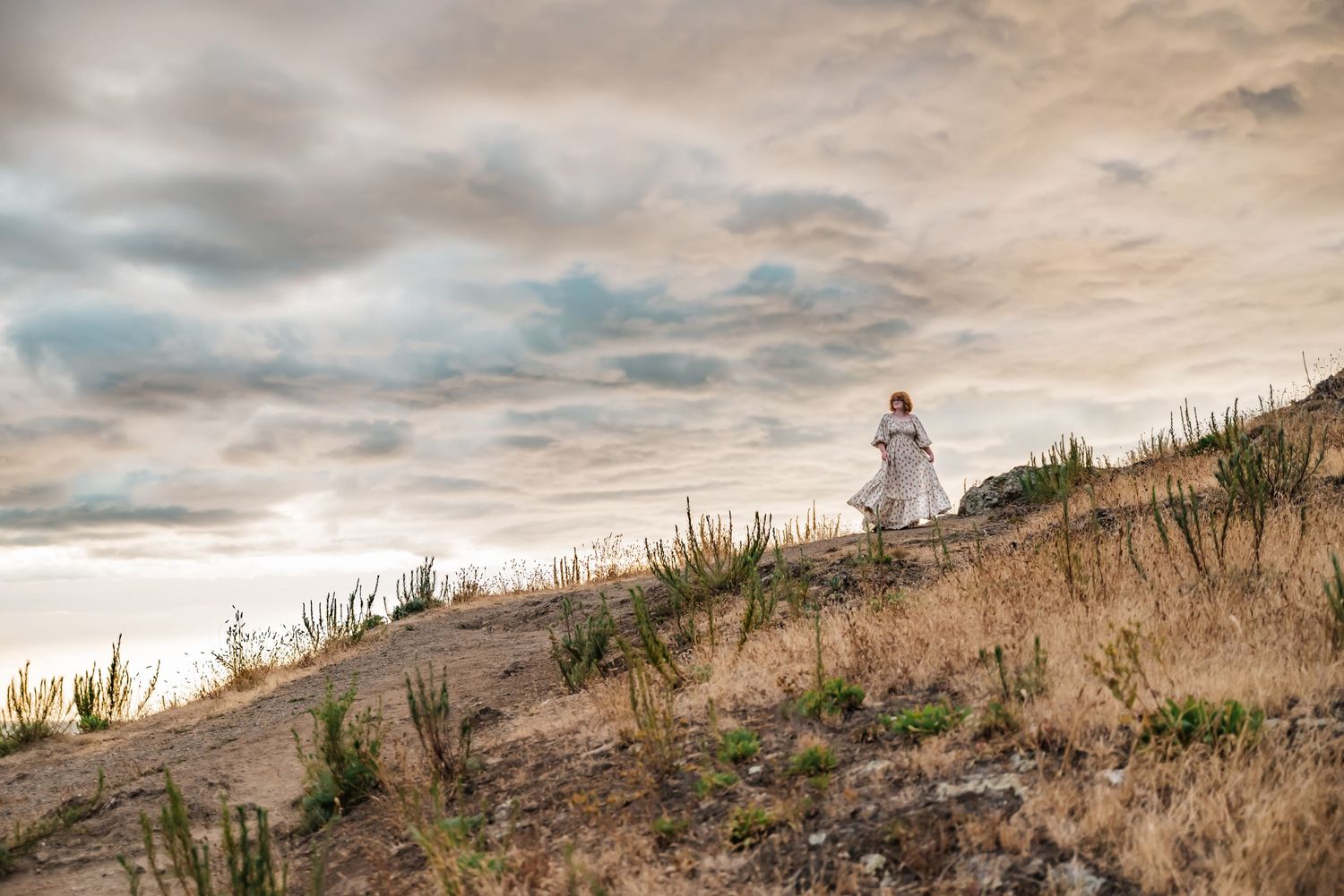 senior girl in flowing dress on hill backed by stunning summer sky