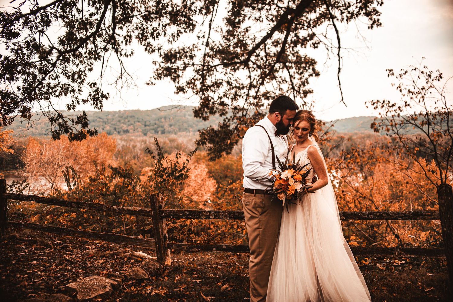 Wedding couple embracing against autumn landscape with orange foliage.