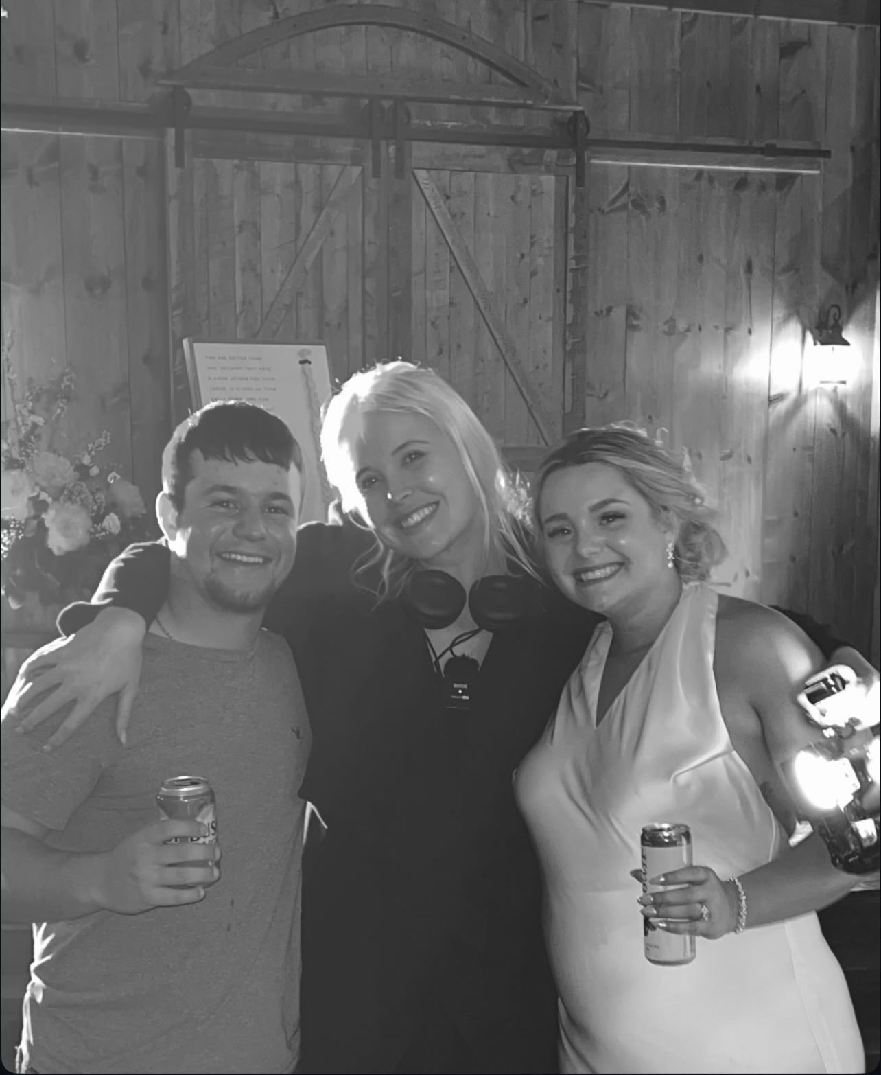 Three people posing together at a casual gathering, holding drinks and smiling in black and white photography.