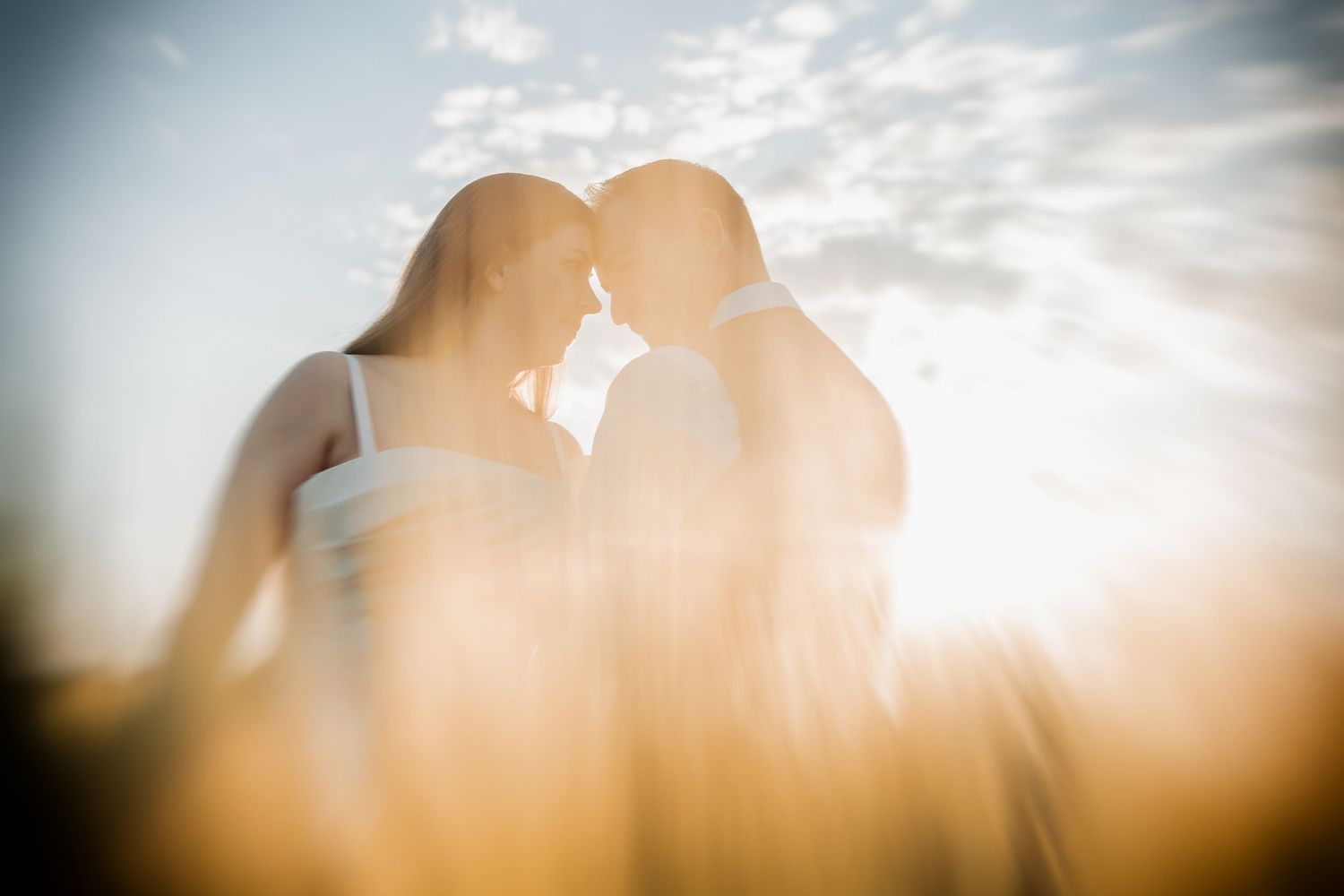 Two people in white outfits standing together among tall grasses near trees in a dreamy outdoor setting.