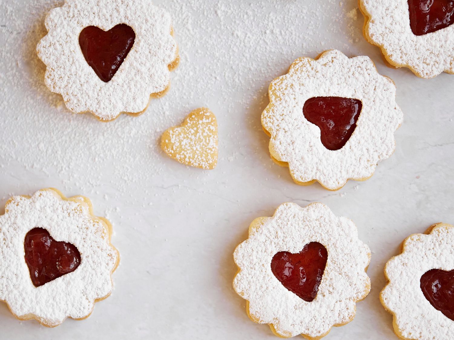 Traditional Linzer cookies with heart-shaped centers filled with red jam and dusted with powdered sugar.