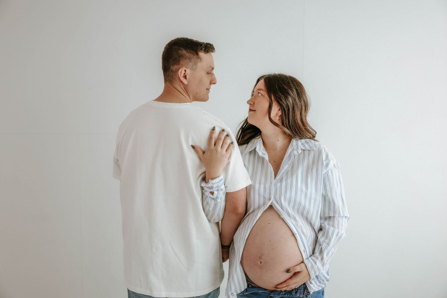 Expectant couple shares intimate moment against white wall as they anticipate their baby's arrival.