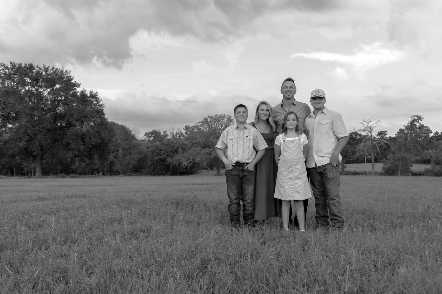 Black and white portrait of a family standing together in an open field with trees in the background.