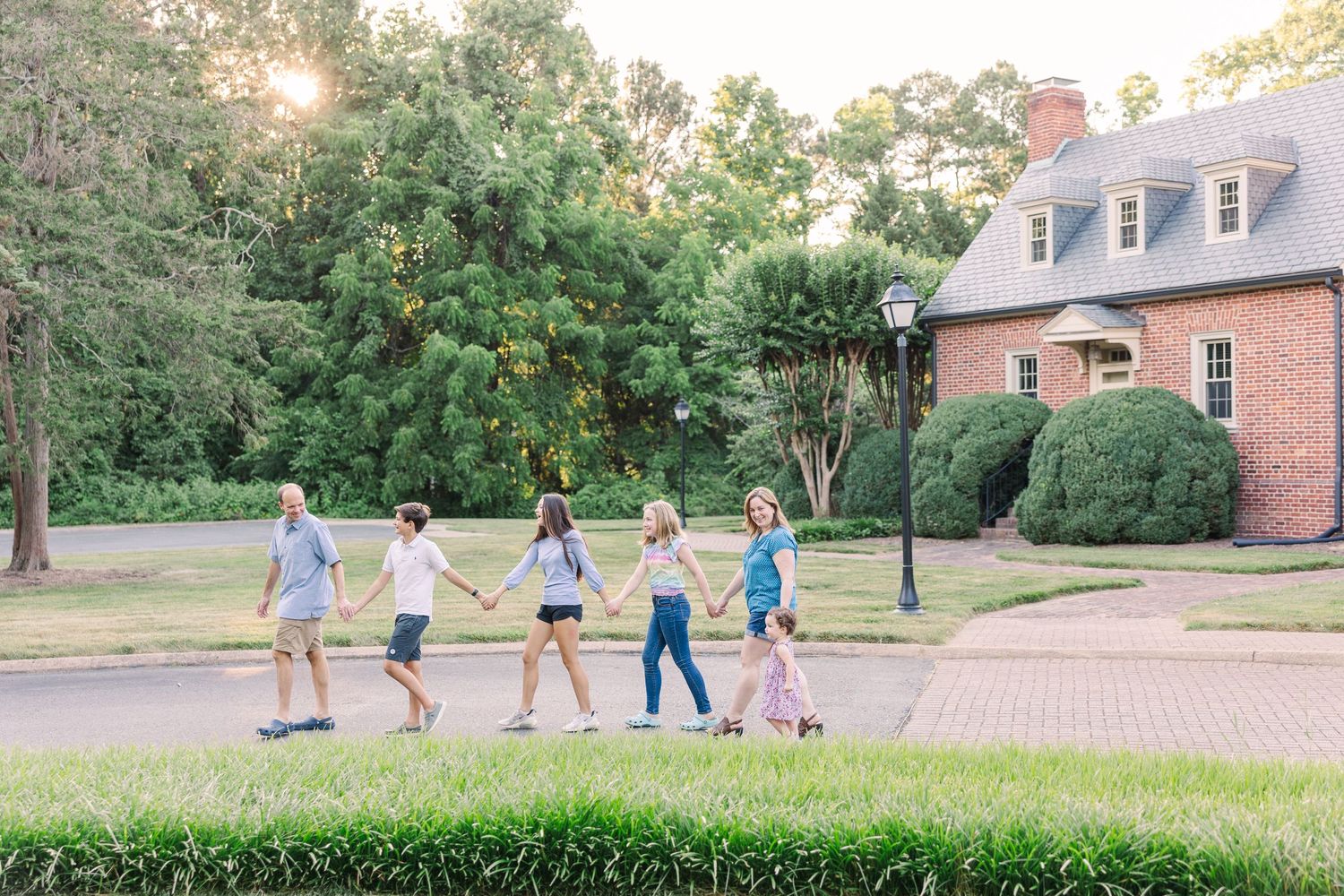 family of 6 holding hands and walking in a line smiling at each other in the sunset
