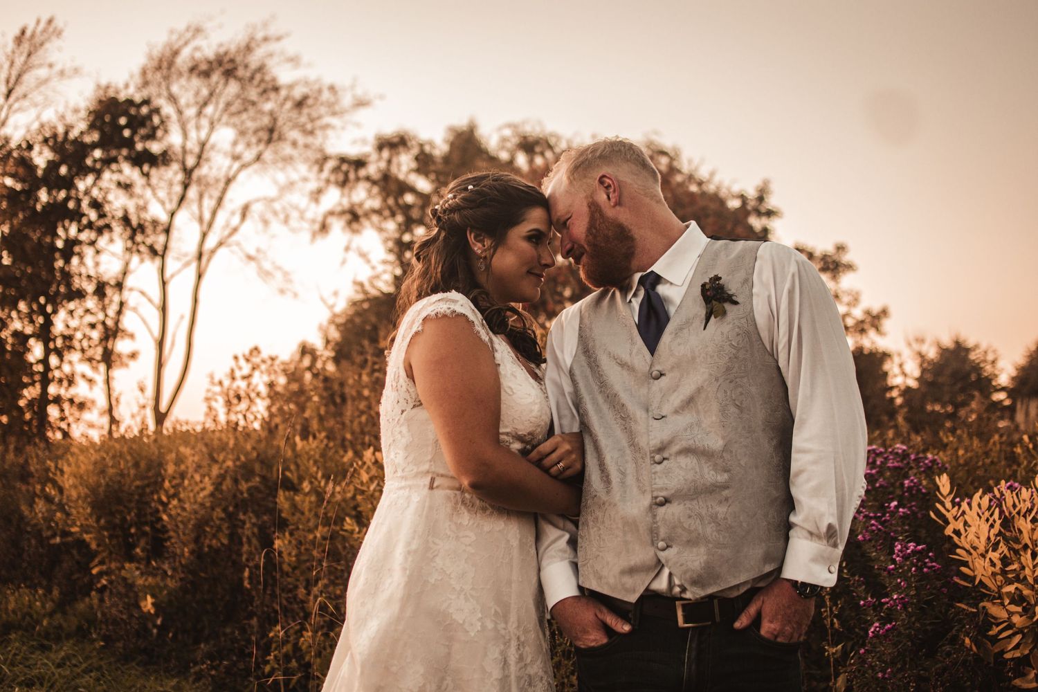 A romantic sunset wedding portrait featuring warm autumn colors and golden light filtering through trees.