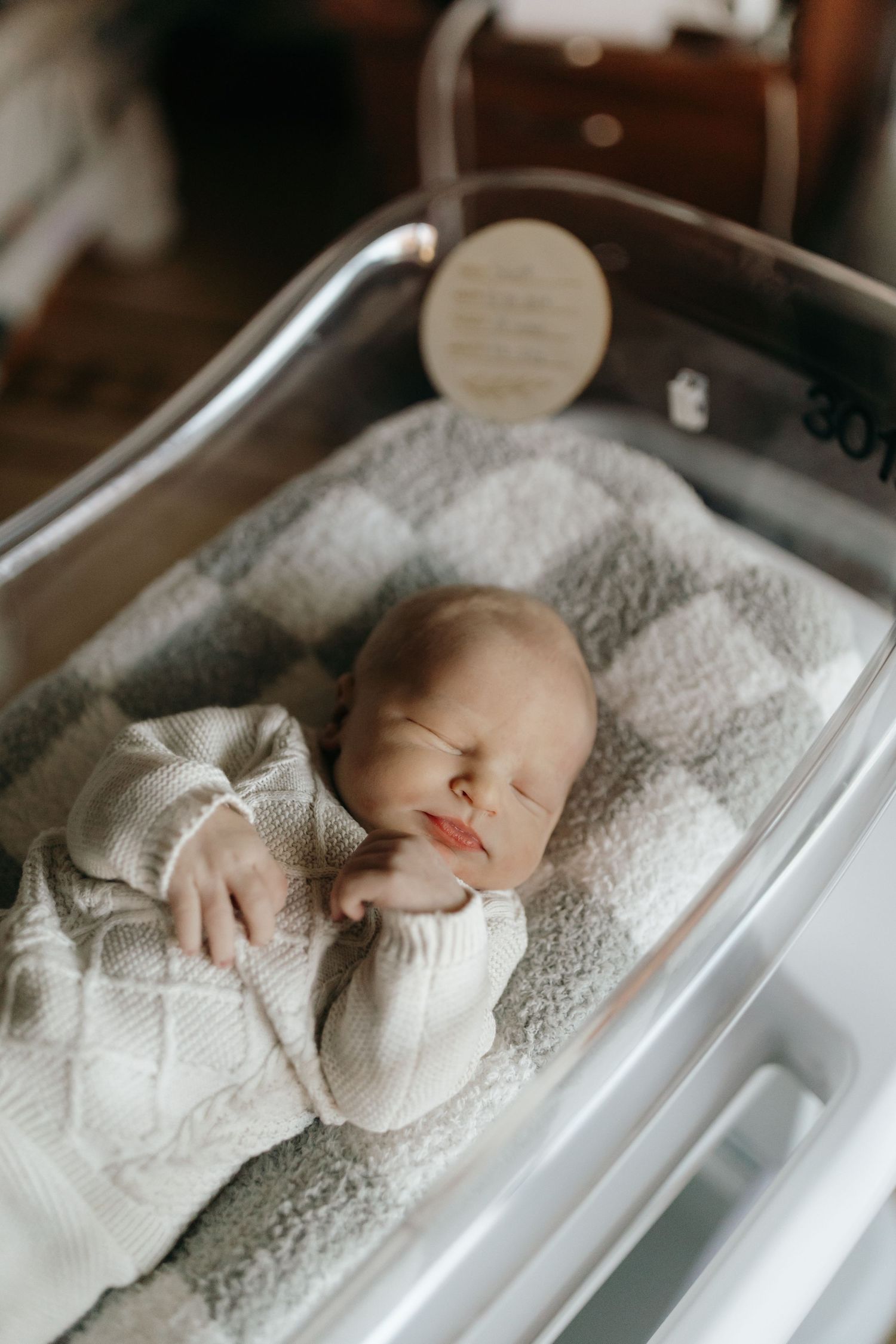 A peaceful newborn baby sleeping in a hospital bassinet wrapped in soft white blankets.
