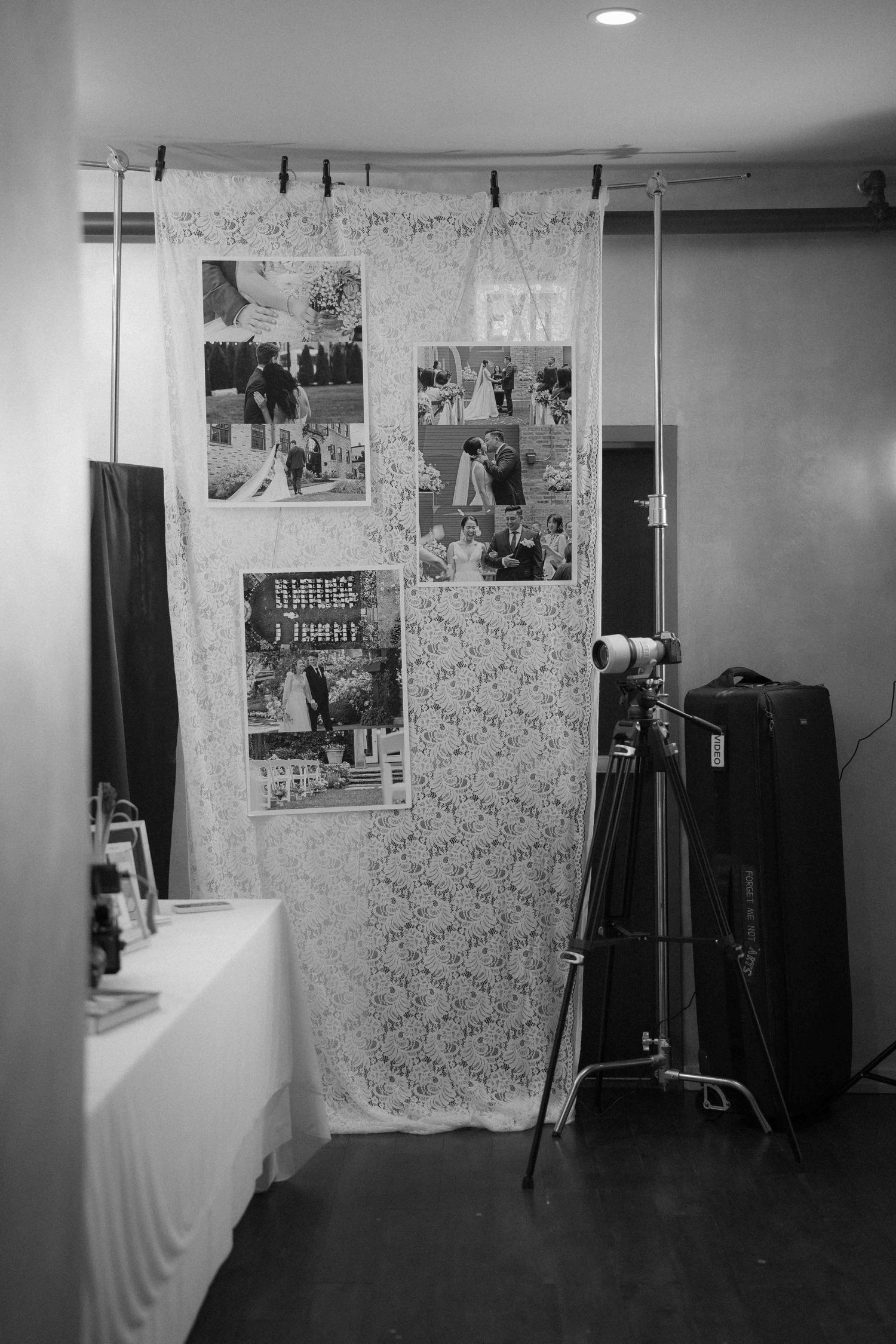Black and white photo of a photo display wall with lace backdrop and photography equipment.
