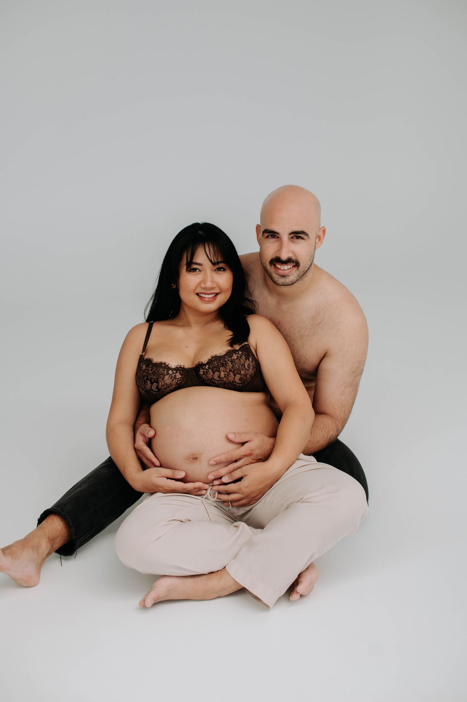 Intimate couples maternity photo against light gray backdrop.