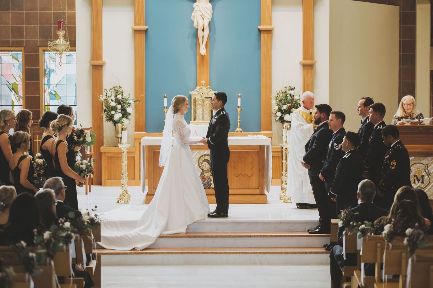 A traditional catholic church wedding ceremony takes place at the altar with guests seated in wooden pews.