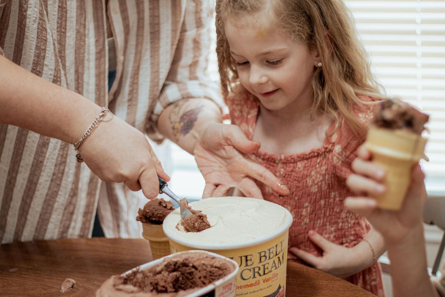 Someone scoops chocolate cookie butter spread onto a plate while a child holds the jar and smiles in anticipation.