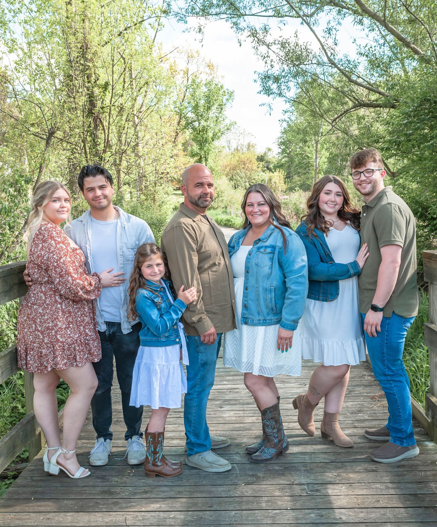 A family group poses together on a wooden bridge surrounded by spring greenery.
