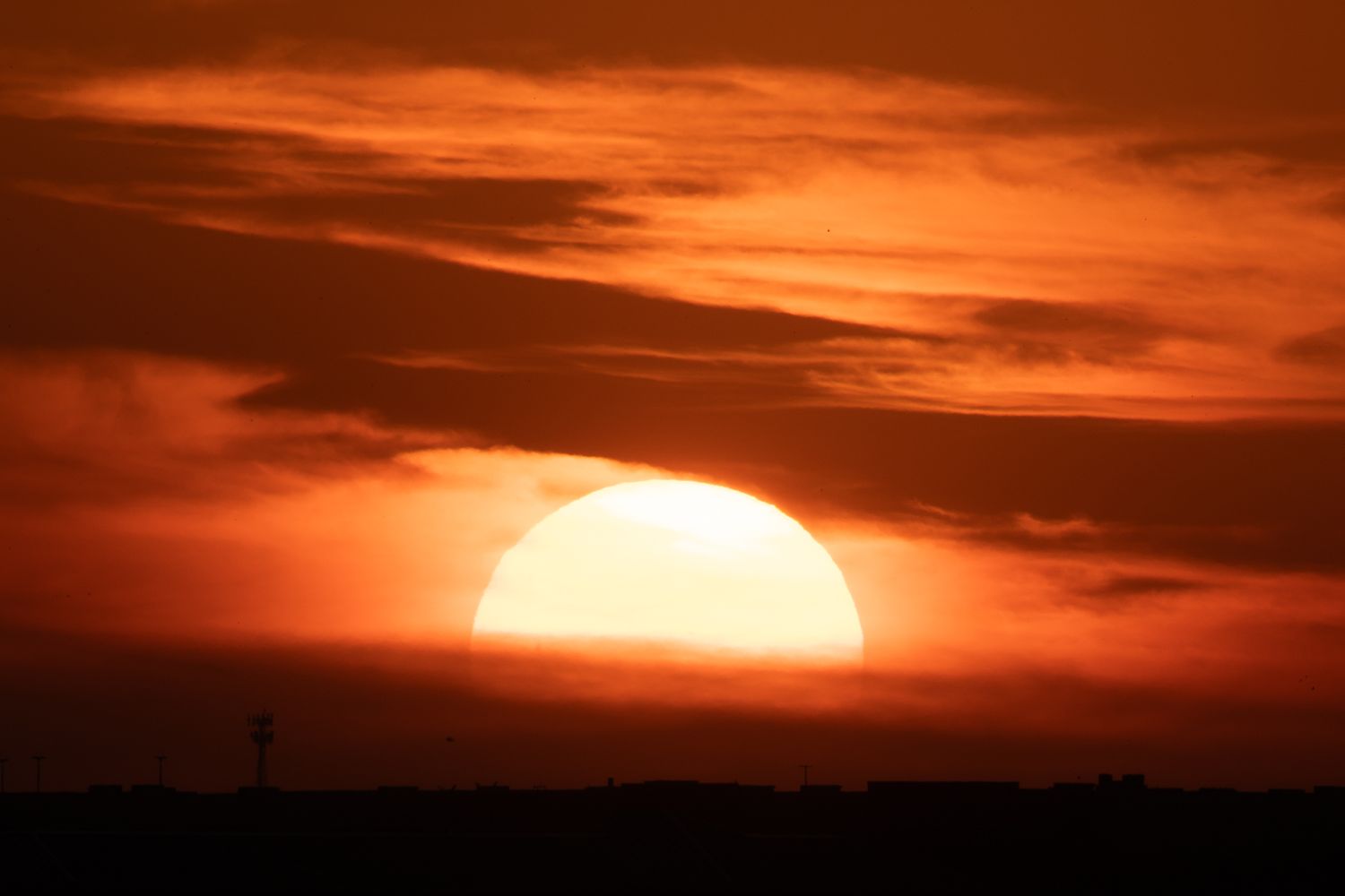 Dramatic orange sunset with large sun partially visible through clouds.
