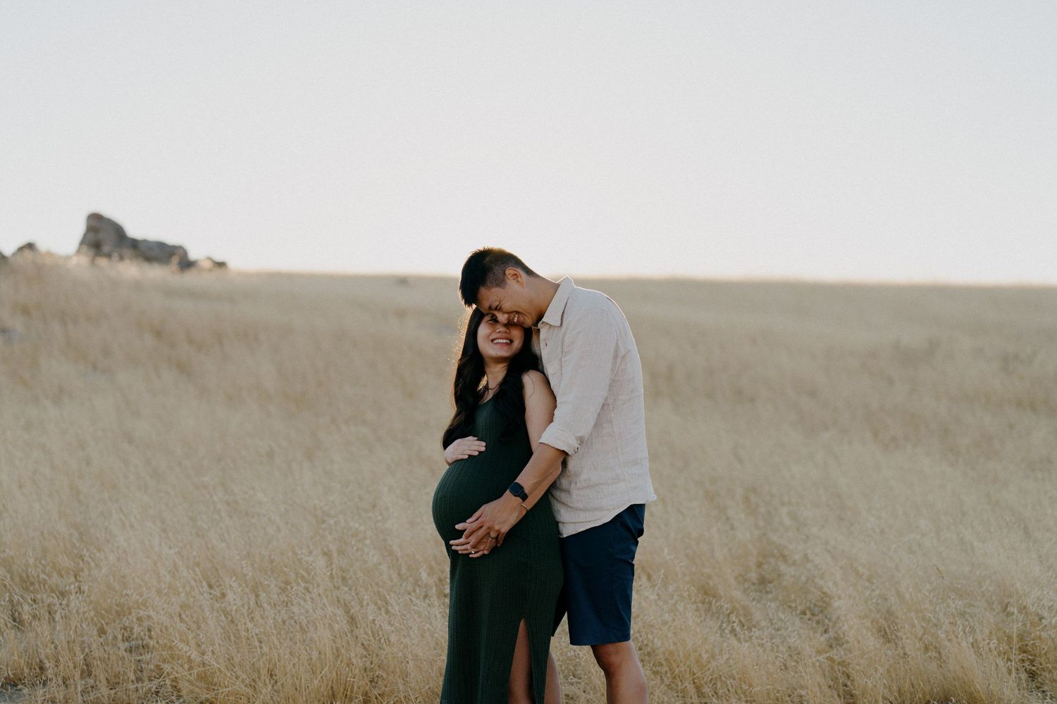 A tender maternity moment captured against a backdrop of golden grass.