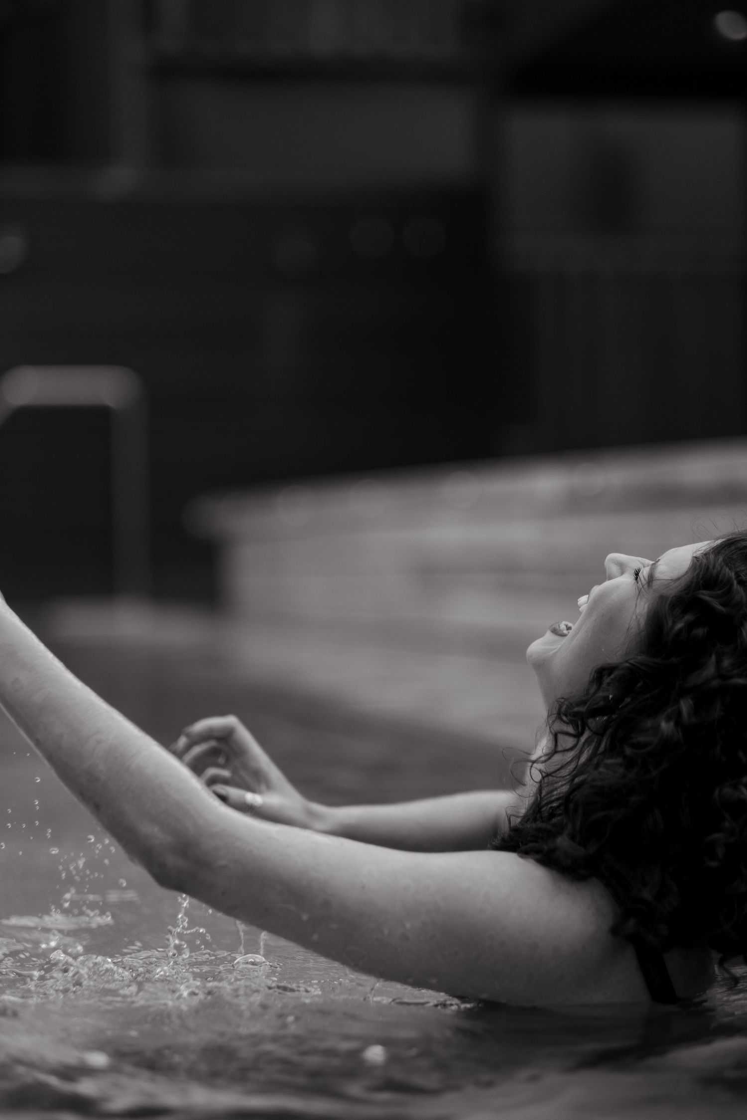 a woman laughes and splashes water around her in a pool at Ellery Beach House Lidingö while being captured by Stockholm photographer